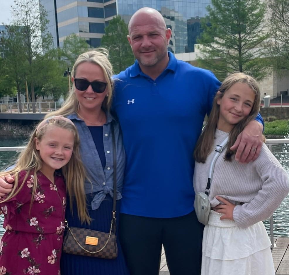 Family of four posing outdoors near water and city buildings.