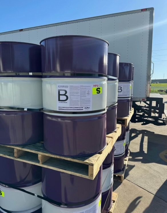 Close-up of purple and white industrial barrels labeled B beside truck.