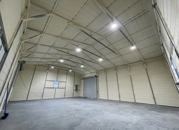 Large empty warehouse interior with metal walls, concrete floor, and overhead lights.